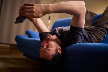 Chilled man on sofa, Casual individual reclining on sofa engrossed with mobile device, Unwinding man sits comfortably on sofa focused on his smartphone amid cozy modern decor