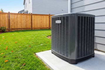 Modern residential air conditioning unit on concrete pad next to house siding in sunny backyard
