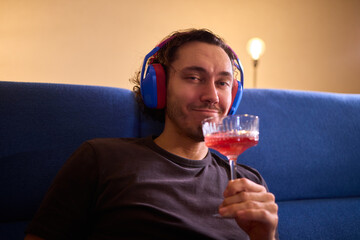 Relaxed man enjoying wine, Person wearing headphones rests peacefully, Creative professional enjoys evening relaxation with wine and soothing music in modern living space © Евгений Вершинин