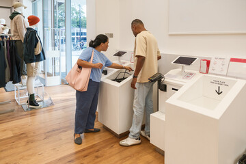 Customers use self-checkout system in clothing store during busy shopping day in city center