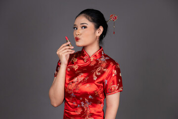 Fototapeta premium Elegant Asian Woman Applying Lipstick in Traditional Attire