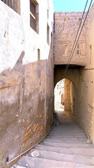 Dark Path Journey, Old Stone Corridor Under Arched Roof, Shadowy Passageway Shaded By Ancient Stone Structures Beneath Sunlight, Dim Alleyway Featuring Aged Walls And Cautious Leader Under Bright Sky