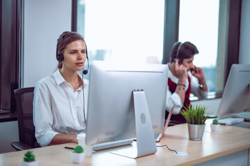 Female customer support agent wearing headset working at computer in modern office, calm expression showing attentive listening and professional service role