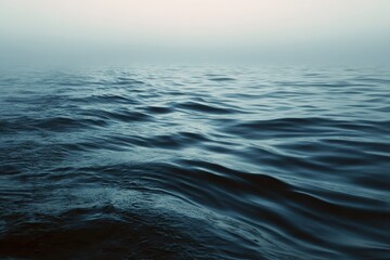 Obraz premium Morning fog blankets serene sea ripples, creating a tranquil atmosphere over calm waters at dawn