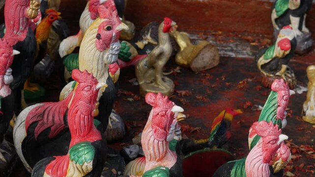 Group of colorful rooster statues as offerings at Thai spirit house or temple shrine, traditional religious belief and superstition concept.