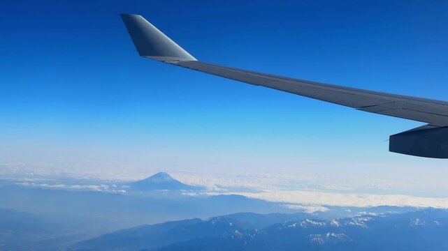 Plane wing and Mount Fuji seen from an airplane on a beautiful blue day with snow on the peak.