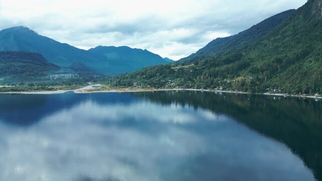 Panning drone aerial of Ranco Lake with mirror reflections, dramatic mountains valley backdrop, moody sky, and Chilean wilderness