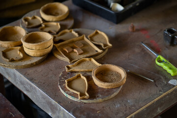 Handcrafted clay pottery pieces on workbench, showcasing various shapes and designs. artisan tools and workspace reflect creative atmosphere
