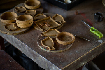 Handcrafted clay pottery pieces on wooden table, showcasing various shapes and textures. workspace is filled with tools and materials, reflecting artistry of pottery making