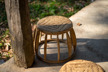 woven bamboo stool placed on concrete surface, surrounded by greenery, showcasing rustic design and natural materials. sunlight casts shadows, enhancing its texture