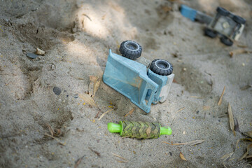 blue toy truck and green toy roller lie on sandy ground, surrounded by small leaves. scene captures playful moment in child outdoor play area