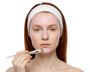 Beautiful woman applying pink clay mask with brush, isolated on white