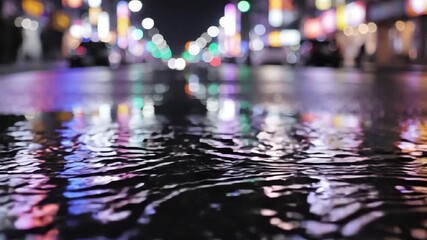 Raindrops hitting the wet city street pavement causing beautiful ripples at night