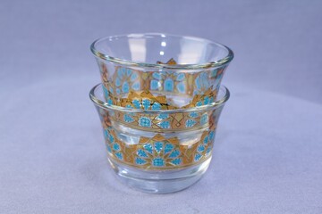 Two stacked clear glass traditional Arabic coffee cups finjan with blue and 22K gold geometric pattern design