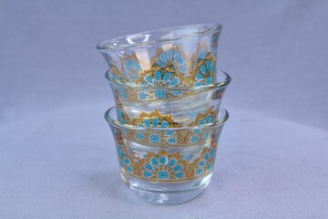 Three stacked clear glass traditional Arabic coffee cups finjan with blue and 22K gold geometric pattern design
