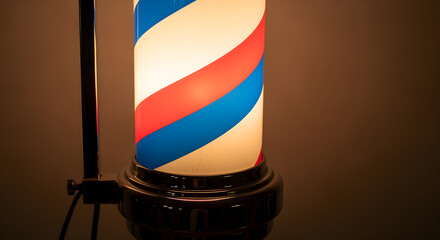 Illuminated barber pole against a neutral backdrop, featuring alternating colored stripes. Warm light gives a vintage ambiance