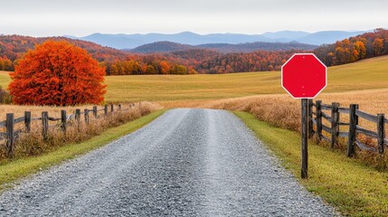 A country road with a stop sign, fenced fields, autumn trees, and mountains in the distance under an overcast sky.