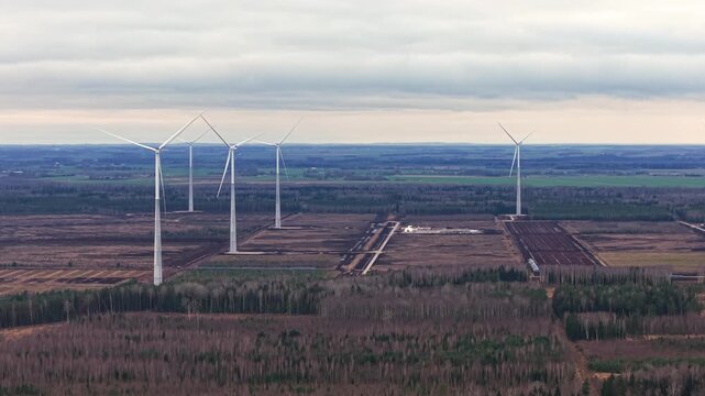 Aerial establishing of multiple wind turbines aligned across flat countryside, medium tracking right