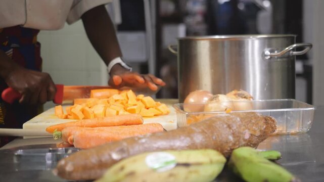 Detailed slow-motion sequence captures a chef's professional knife skills while dicing orange-fleshed yams for a traditional soup base on a professional kitchen setting.