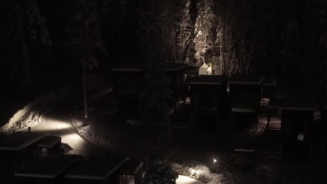 A woman pulling curtains inside cozy glass cabin at a winter night, Lapland