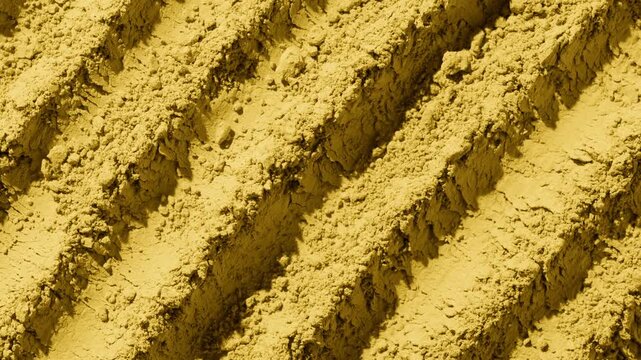 Overhead frame of yellow powder furrows surface illuminated by orbiting directional light casting dynamic shadows