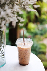 Fresh a plastic glasses of ice latte coffee and dry grass flower in vase decorated on white table for outdoors garden