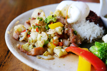 Close up stir-fried pork with cauliflower with boiled egg, fish sauce, broccoli and raspberry rice on a white plate