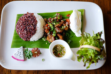 Top view of brown rice berry stir-fried boiled eggs with basil and vegetables on fresh banana leaf on white dish. Traditional Thai food