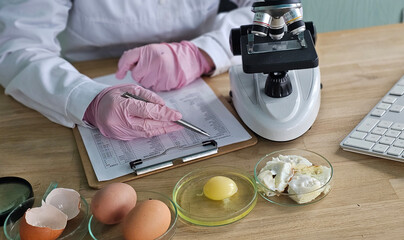 Researcher conducts food analysis in laboratory on eggs and dairy with microscope and data sheet for study on nutrition concept