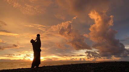 Silhouette of a happy father lifting his little child high up in the air on the beach during a...