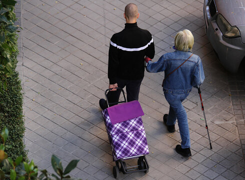 Hijo con madre agarrada del brazo con bast&oacute;n y carro en perspectiva a&eacute;rea