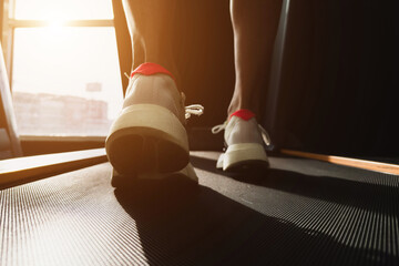 Young athlete wearing white sport shoes running on treadmill. He training for cardiovascular endurance and good health with personal trainer in fitness center.