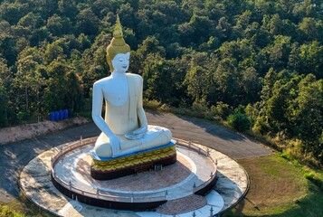Drone close-up of a white Buddha statue with golden headpiece in the forest, Thailand