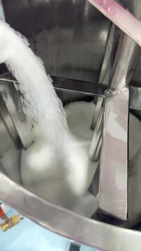 Close-up footage of white powder being poured into a stainless steel industrial mixing tank with an agitator. Concept of factory manufacturing, formulation, blending, and ingredient.