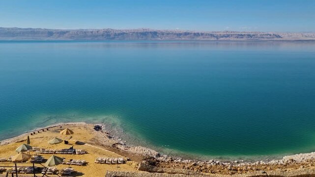 Wide panorama over the Dead Sea in Jordan, revealing turquoise waters and a rugged shoreline, the shrinking coastline highlights environmental change driven by climate change and intensive agriculture