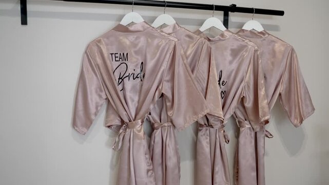 Four matching robes hang neatly on a rack. Each robe shows the words Team Bride. The room is bright and ready for the special day ahead. Friends gather to celebrate together.
