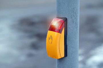 Pedestrian crossing button with illuminated red signal on a pole in winter urban environment, close-up traffic safety detail.