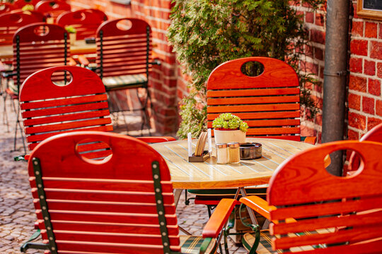 Bright red chairs surround a wooden table adorned with potted plants in a cozy outdoor setting - Powered by Adobe