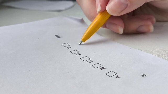 A woman's hand holds a pen and thinks about which answer to choose in the exam test. The process of exams in schools, universities, colleges. Training, education