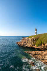 vertical panoramic view of the black and white lighthouse standing on a rocky cliff by the deep blue sea under a clear sky, Isla de Pancha, Ribadeo, Galicia, Spain
