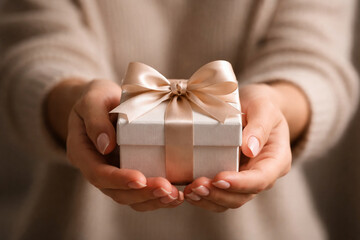 Close-up of hands holding a small white gift box with a light pink ribbon and bow.