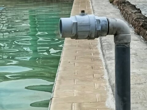 PVC water pipe valve on the edge of a swimming pool. Close-up of pool filtration system and plumbing equipment for maintenance, aquatic facility, and industrial concepts.