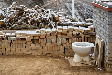 Basic white ceramic toilet fixture with stacked construction materials and firewood