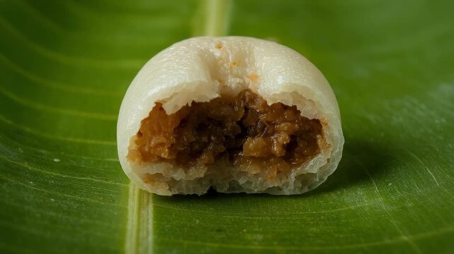 A close-up shot of a traditional steamed rice cake, similar to Indonesian Kue Bugis or Klepon, featuring a soft white chewy texture and a sweet brown palm sugar coconut filling inside.