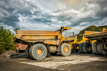 Large quarry dump truck. Big yellow mining truck at work site under cloudy sky