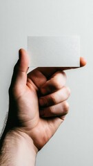 A hand holding a blank white business card between the thumb and index finger. Concept Hand-held blank business card, Close-up of fingers, Minimalist white card, Professional branding prop