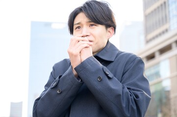 冬のオフィス街で寒そうな日本人男性