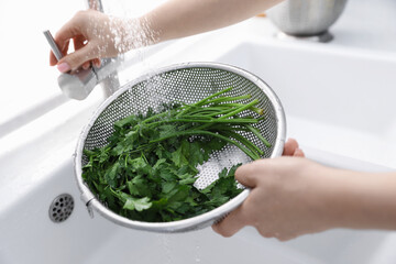 Woman washing parsley in sieve at sink, closeup