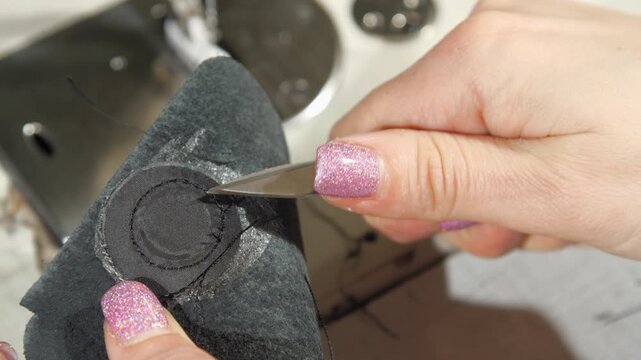 Woman with bright manicure performs work using special scissors. Seamstress cuts excess threads on processed fabric with help of working tool