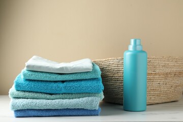 Laundry basket with towels and bottle of detergent on light table near beige wall indoors
